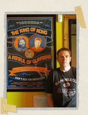 'Philip posing with a movie poster from The King of Kong in Funspot